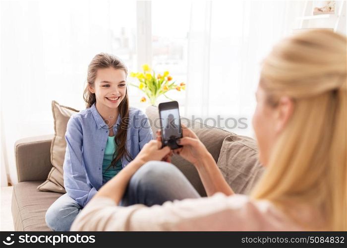 family, technology and people concept - happy mother and daughter with smartphone taking photo at home. happy family taking photo by smartphone at home. happy family taking photo by smartphone at home