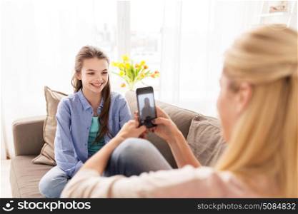 family, technology and people concept - happy mother and daughter with smartphone taking photo at home. happy family taking photo by smartphone at home. happy family taking photo by smartphone at home