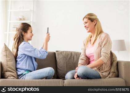 family, technology and people concept - happy mother and daughter with smartphone taking photo at home. happy family taking photo by smartphone at home