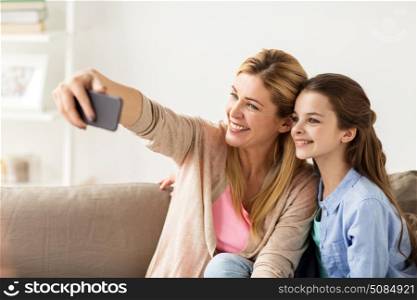 family, technology and people concept - happy mother and daughter with smartphone taking selfie at home. happy family taking selfie by smartphone at home. happy family taking selfie by smartphone at home