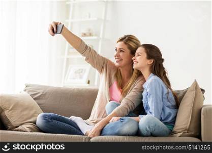 family, technology and people concept - happy mother and daughter with smartphone taking selfie at home. happy family taking selfie by smartphone at home