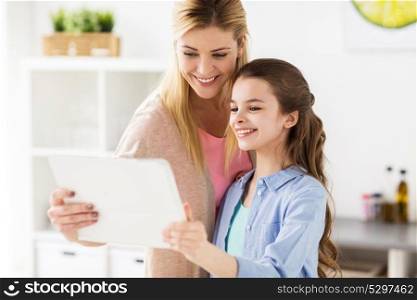 family, technology and people concept - happy mother and daughter with tablet pc computer at home kitchen. happy family with tablet pc computer at kitchen