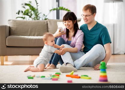 family, technology and people concept - happy mother and father taking picture or recording video of baby boy with smartphone at home. happy family with baby boy at home
