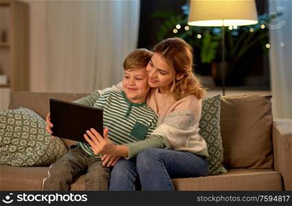 family, technology and people concept - happy mother and little son sitting on sofa and using tablet pc computer at home. mother and son using tablet computer at home