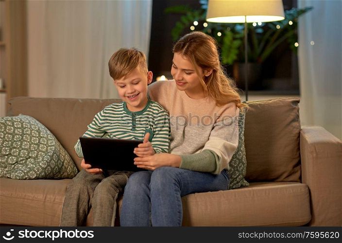 family, technology and people concept - happy mother and little son sitting on sofa and using tablet pc computer at home. mother and son using tablet computer at home