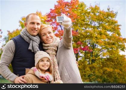 family, technology and people concept - happy mother, father and daughter taking selfie by camera over autumn park background. family taking selfie by camera in autumn park