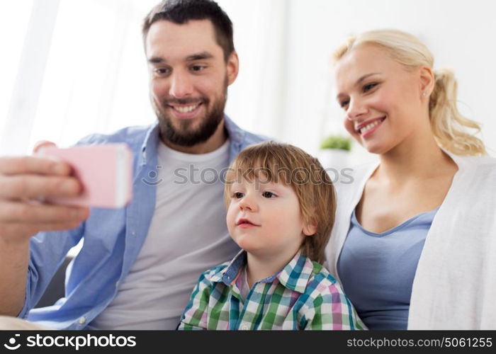 family, technology and people concept - happy mother, father and little boy with smartphone at home. happy family with smartphone at home