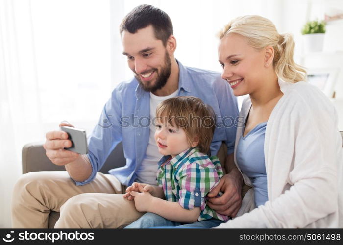 family, technology and people concept - happy mother, father and little boy with smartphone at home. happy family with smartphone at home