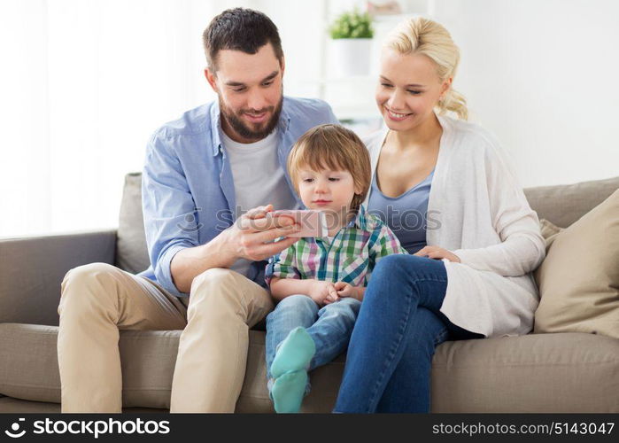 family, technology and people concept - happy mother, father and little boy with smartphone at home. happy family with smartphone at home