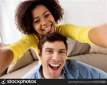 family, technology and people concept - happy multiethnic couple taking selfie and having fun at at home. happy multiethnic couple taking selfie at home