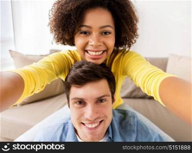 family, technology and people concept - happy multiethnic couple taking selfie at home. happy multiethnic couple taking selfie at home