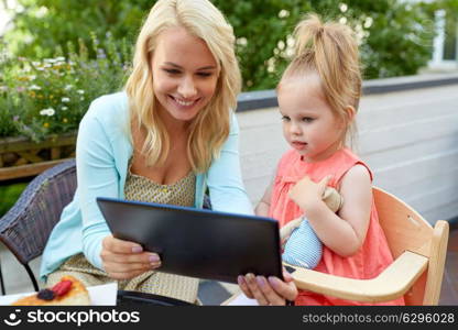 family, technology and people concept - happy smiling mother and daughter with tablet pc computer at cafe or restaurant terrace. mother and daughter with tablet pc at cafe terrace