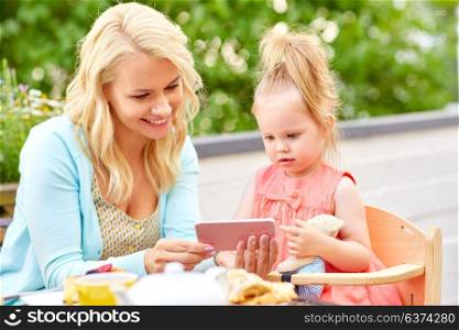 family, technology and people concept - happy smiling mother and daughter with smartphone at cafe or restaurant terrace. mother and daughter with smartphone at cafe