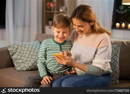 family, technology and people concept - happy smiling mother and little son sitting on sofa and using smartphone at home. mother and son using smartphone at home