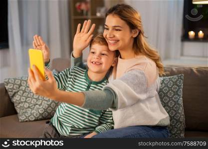 family, technology and people concept - happy smiling mother and little son with smartphone having video call and waving hands at home. mother and son with smartphone having video call