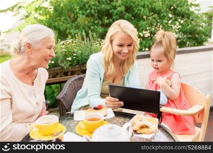family, technology and people concept - happy smiling mother, daughter and grandmother with tablet pc computer at cafe or restaurant terrace. mother, daughter and grandmother with tablet pc