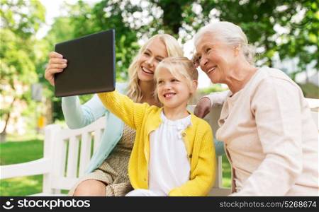 family, technology and people concept - happy smiling woman, little daughter and senior mother with tablet pc computer sitting on park bench. mother, daughter and grandmother with tablet pc