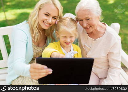 family, technology and people concept - happy smiling woman, little daughter and senior mother with tablet pc computer sitting on park bench. mother, daughter and grandmother with tablet pc