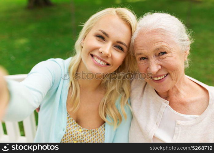 family, technology and people concept - happy smiling young daughter and senior mother sitting on park bench and taking selfie. daughter and senior mother taking selfie at park