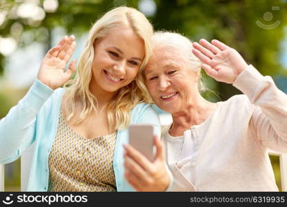 family, technology and people concept - happy smiling young daughter and senior mother with smartphone sitting on park bench and taking selfie. daughter and senior mother taking selfie at park
