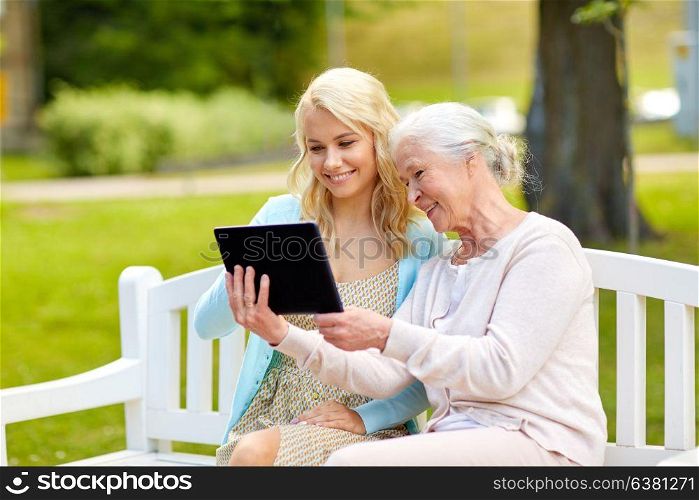family, technology and people concept - happy smiling young daughter and senior mother with tablet pc computer sitting on park bench. daughter and senior mother with tablet pc at park