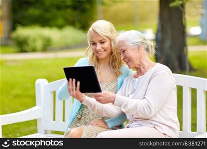 family, technology and people concept - happy smiling young daughter and senior mother with tablet pc computer sitting on park bench. daughter and senior mother with tablet pc at park