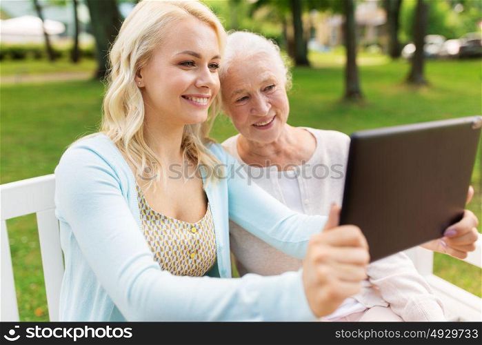 family, technology and people concept - happy smiling young daughter with tablet pc computer and senior mother sitting on park bench. daughter with tablet pc and senior mother at park
