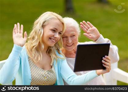 family, technology and people concept - happy smiling young daughter with tablet pc computer and senior mother on park bench waving hands. daughter with tablet pc and senior mother at park