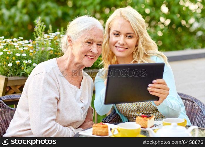 family, technology and people concept - happy smiling young daughter with tablet pc computer and senior mother at cafe or restaurant terrace. daughter with tablet pc and senior mother at cafe