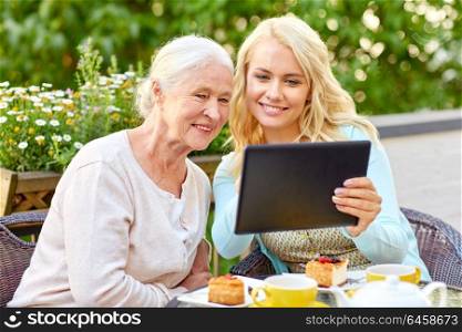 family, technology and people concept - happy smiling young daughter with tablet pc computer and senior mother at cafe or restaurant terrace. daughter with tablet pc and senior mother at cafe