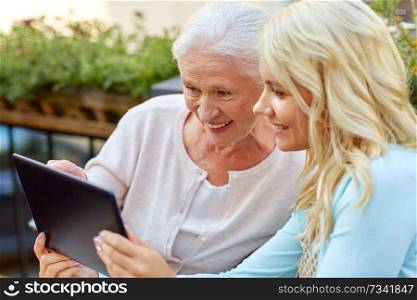 family, technology and people concept - happy smiling young daughter with tablet pc computer and senior mother outdoors. daughter with tablet pc and senior mother outdoors