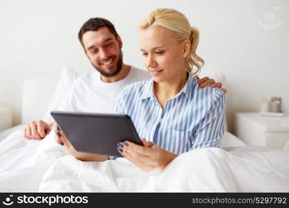 family, technology and people concept - smiling happy couple with tablet pc computer in bed at home bedroom. smiling happy couple with tablet pc in bed at home