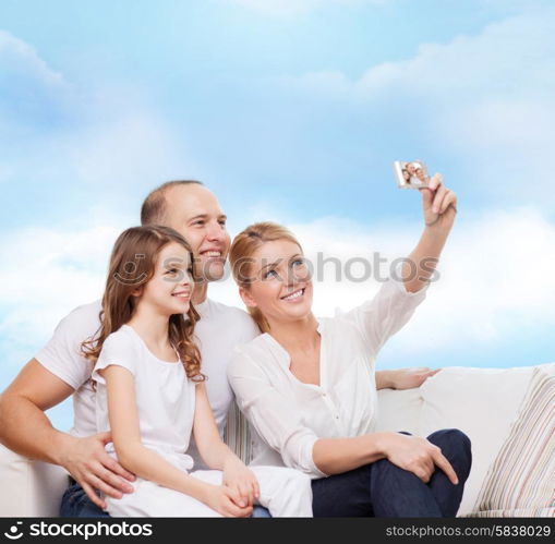 family, technology and people concept - smiling mother, father and little girl making selfie with camera over blue sky background