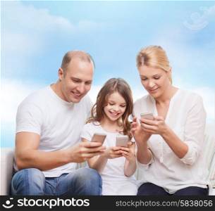 family, technology and people concept - smiling mother, father and little girl with smartphones over blue sky background
