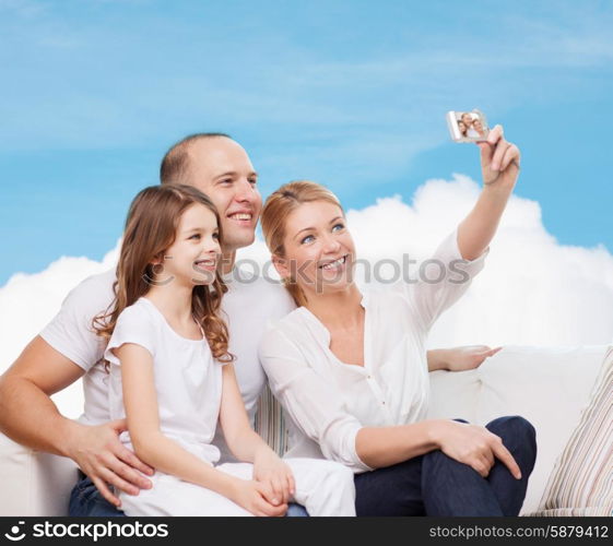 family, technology and people concept - smiling mother, father and little girl making selfie with camera over blue sky and white cloud background