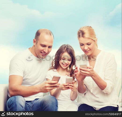 family, technology and people concept - smiling mother, father and little girl with smartphones over blue sky background