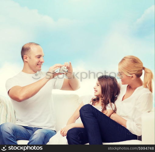 family, technology and people - smiling mother, father and little girl with camera over blue sky background