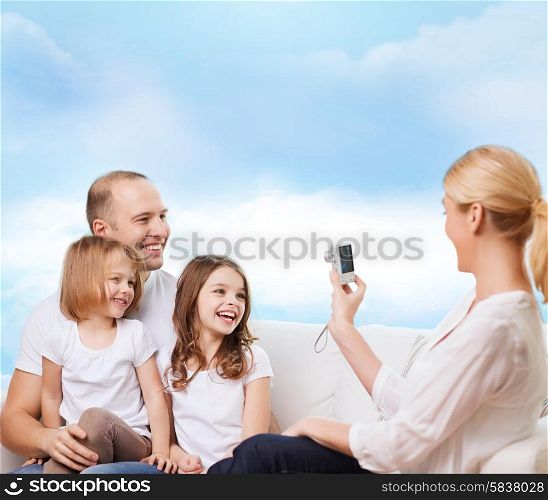 family, technology and people - smiling mother, father and little girls with camera over blue sky background