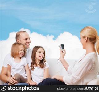 family, technology and people - smiling mother, father and little girls with camera over blue sky and white cloud background
