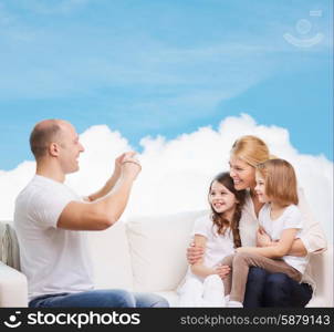 family, technology and people - smiling mother, father and little girls with camera over blue sky and white cloud background