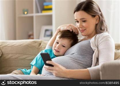 family, technology and pregnancy concept - happy pregnant mother and little son with smartphone at home. pregnant mother and son with smartphone at home