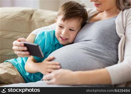 family, technology and pregnancy concept - happy pregnant mother and little son with smartphone at home. pregnant mother and son with smartphone at home