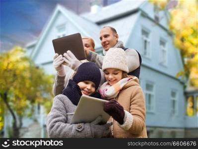 family, technology and real estate concept - happy mother, father, daughter and son with tablet pc computers over living house background outdoors in autumn. family with tablet pc over living house in autumn