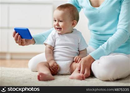 family, technology, child and parenthood concept - close up of happy smiling young mother showing smartphone to little baby at home