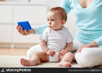 family, technology, child and parenthood concept - close up of young mother showing smartphone to little baby at home