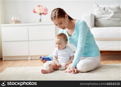 family, technology, child and parenthood concept - happy smiling young mother showing smartphone to little baby at home