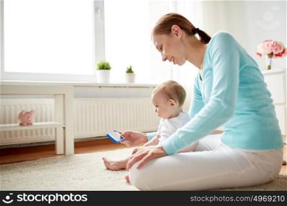 family, technology, child and parenthood concept - happy smiling young mother showing smartphone to little baby at home. happy mother showing smartphone to baby at home