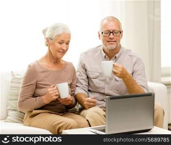 family, technology, drinks, age and people concept - happy senior couple with laptop computer and cups at home