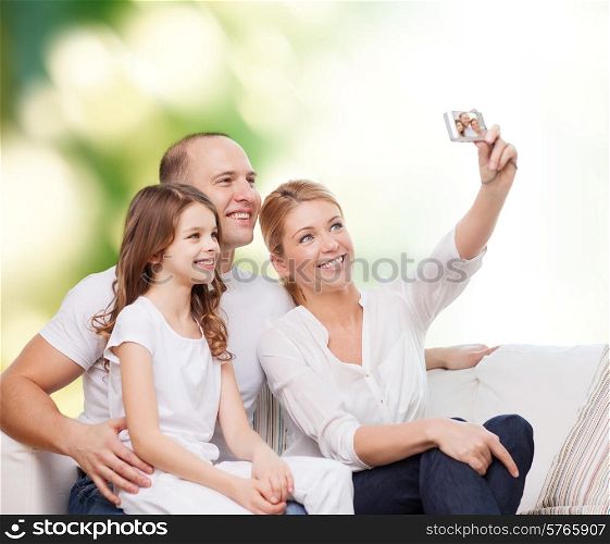 family, technology, ecology and people concept - smiling mother, father and little girl making selfie with camera over green background