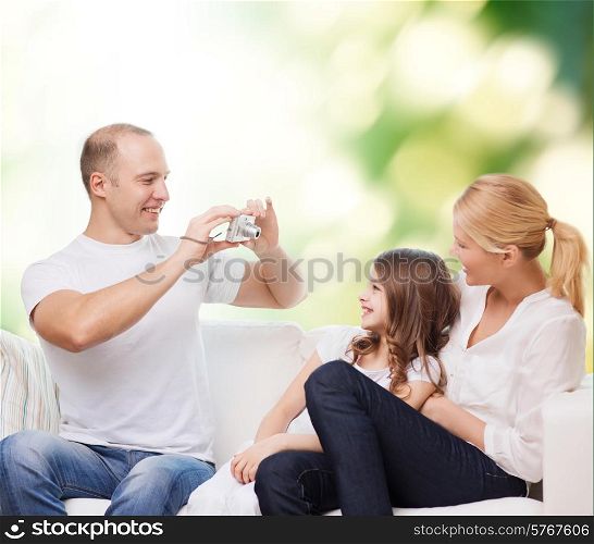 family, technology, ecology and people - smiling mother, father and little girl with camera over green background